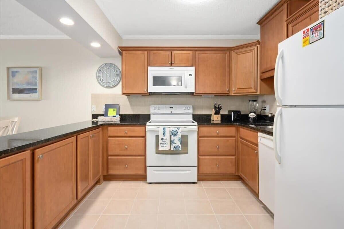 A kitchen with wooden cabinets, a white stove, a microwave, and a refrigerator.