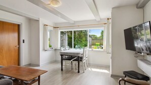 Un salon moderne comprenant un coin repas, un téléviseur fixé au mur et donnant sur le jardin extérieur.