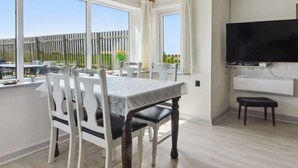 Un espace repas comprenant une table et des chaises, un téléviseur fixé au mur et une vue sur l’extérieur grâce à de grandes fenêtres.
