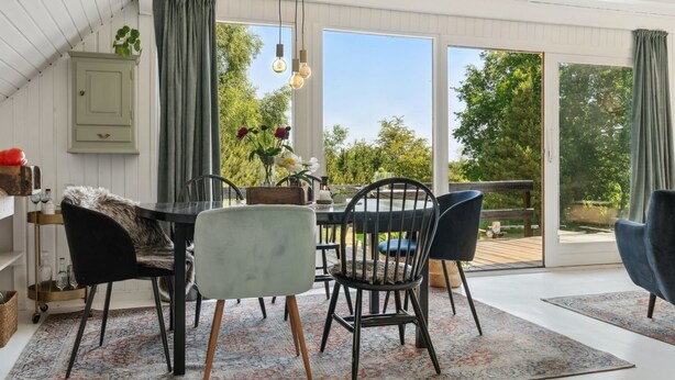 A dining area with a table and chairs, a hanging light fixture, and a view of greenery outside.