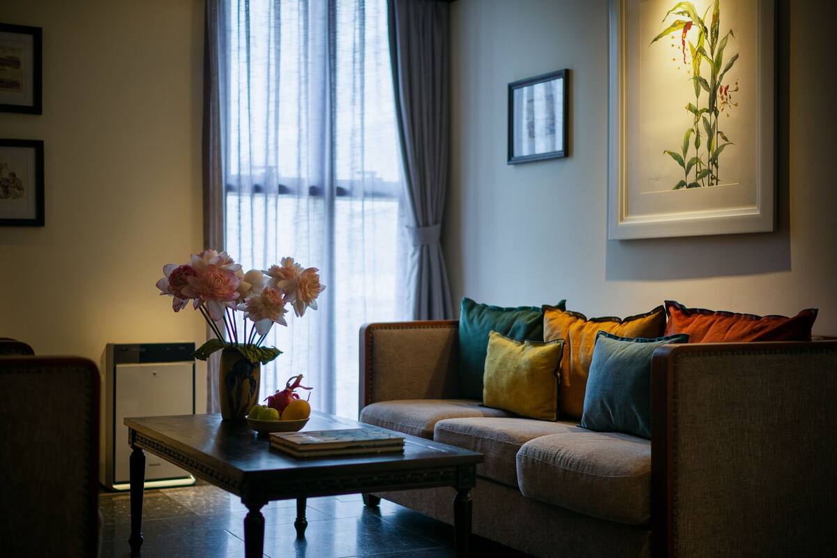A living room with a sofa, a coffee table with a vase of flowers, and a framed botanical print on the wall.