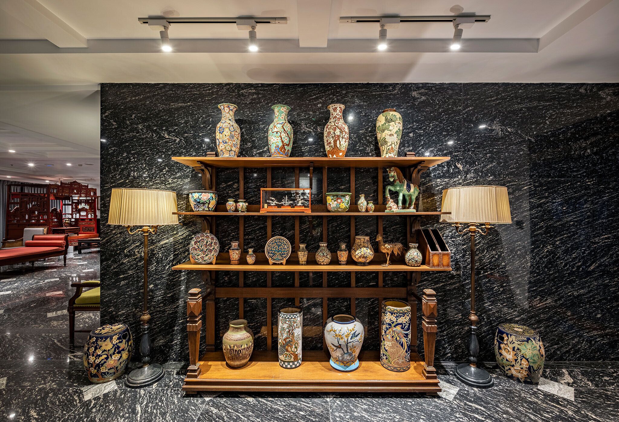 Une collection de vases est exposée sur des étagères, le tout adossé à un mur de marbre dans le hall d’un hôtel.