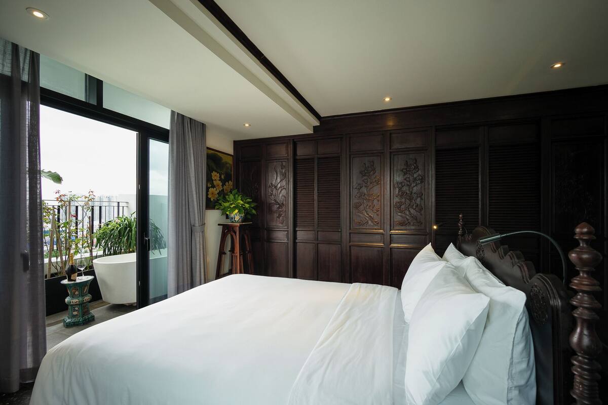 A bedroom with a large bed, dark wood paneling, a potted plant, and a view of the outdoors.
