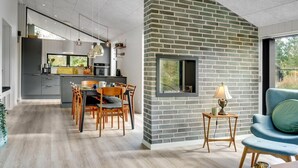A modern kitchen with grey cabinets, a dining area with wooden chairs, and a brick accent wall. - "Sinna" -  from the sea by Interhome (Hals)