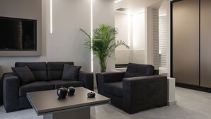 Ein modernes Wohnzimmer mit einem dunkelgrauen Sofa, einem passenden Sessel und einem Couchtisch. Eine große Kühlpflanze und ein Flachbildfernseher an der Wand sind ebenfalls vorhanden.