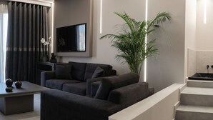 Ein modernes Wohnzimmer mit grauem Sofa, einem flachbildfernseher an der Wand, einer großen Topfpflanze und einer Treppe mit einem schwarzen Waschbecken.