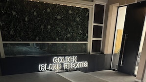 Ein moderner Eingangsbereich des Golden Island Resorts mit einer gut sichtbaren, beleuchteten Schrifttafel, einem sauberen Fliesenboden und einer Wand mit Pflanzenzierde.