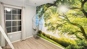 A room with a large window, a hammock, and a mural of a tree with sunlight. - The Stay at Steuben, Fire Pit, Brand new furniture (Springdale)