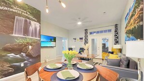 A dining area with a table set for four, a TV mounted on the wall, and a view of a waterfall on the poster. - The Stay at Steuben, Fire Pit, Brand new furniture (Springdale)