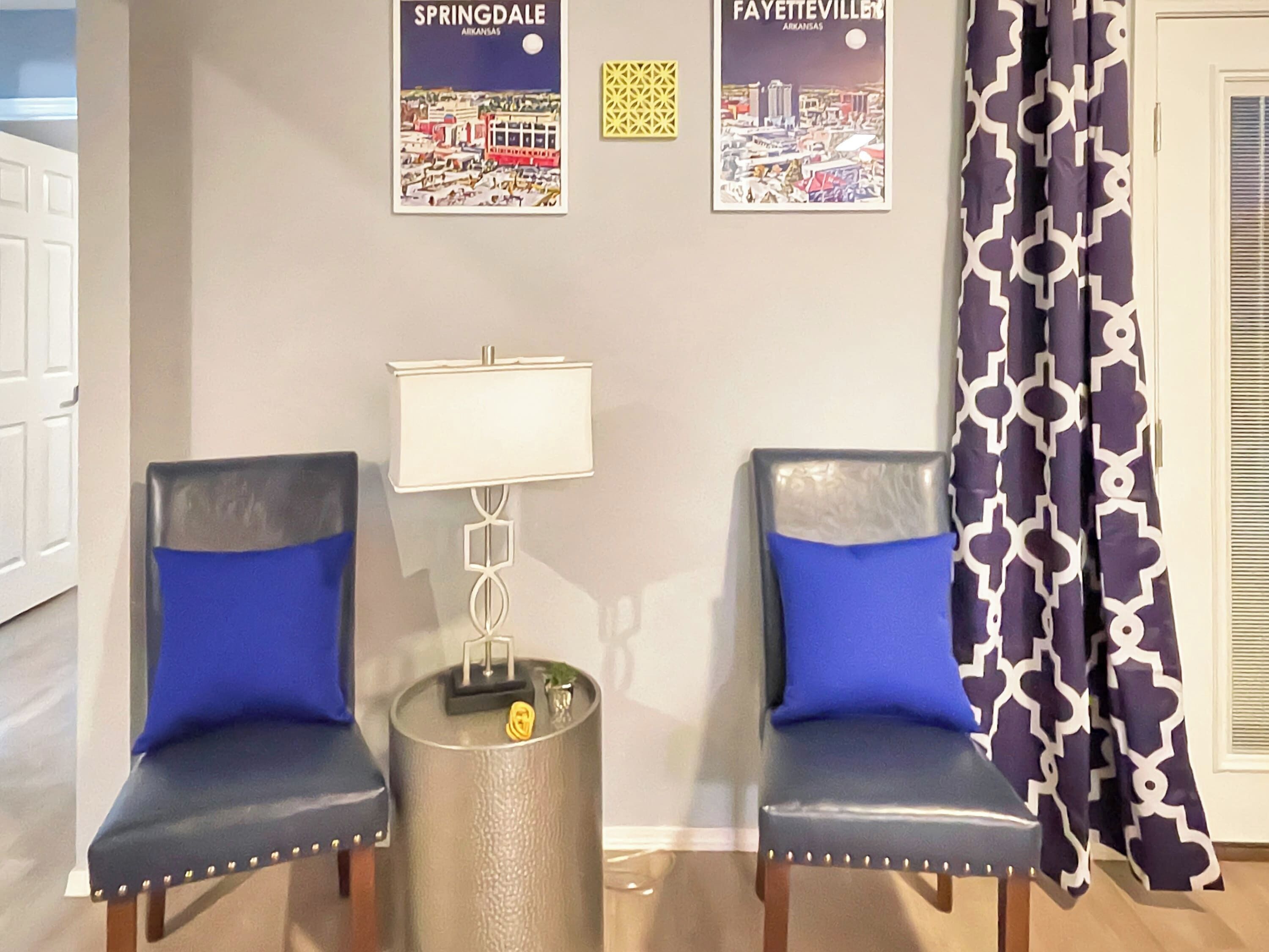Ein Zimmer mit zwei Stühlen, einer Lampe und einem gemusterten Vorhang.