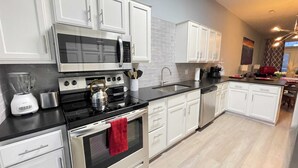 Una cocina moderna con armarios blancos, electrodomésticos de acero inoxidable, una encimera negra y una toalla roja colgada en el horno.