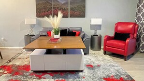 Una sala de estar moderna con una mesa de centro de madera, sofá gris, sillón rojo y un cuadro abstracto grande en la pared.