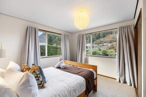 Une chambre à coucher avec un lit, deux fenêtres, une vue sur la ville et un luminaire suspendu.