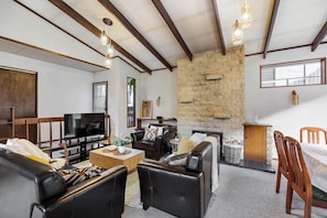 A living room with a stone fireplace, leather sofas, a TV, and hanging lights. - Character Retro Family home in Queenstown (Queenstown)