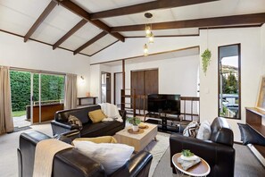 A modern living room with a large TV, leather sofas, a wooden coffee table, and a hanging plant. - Character Retro Family home in Queenstown (Queenstown)