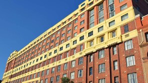 Een meerlaags hotel met een rode en gele gevel, tal van ramen en een helderblauwe lucht op de achtergrond.