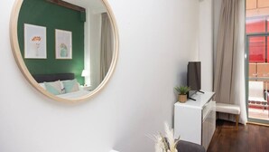 Een kamer met een ronde spiegel, een bed, een bureau met televisie en een raam met gordijnen.