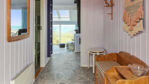 A hallway with a view to a balcony, a wooden bench, a small table, and a wall-mounted decorative piece.