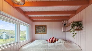 A bedroom with a bed, a window, a painting, and a shelf with plants.