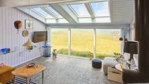A spacious room with a high ceiling, skylights, a large window, and a cozy seating area with a sofa and ottoman.
