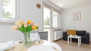 Ett modernt vardagsrum med en matplats för två personer. Här finns ett vitt bord med en vas med tulpaner, en vit soffa och ett litet vitt sidobord.