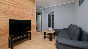 Un saló modern amb televisió de pantalla plana, un panell de paret de fusta, un sofà gris i una taula petita amb una revista.