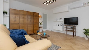 Una sala de estar con un sofá, un televisor, un mueble de madera y una mesita con una planta.