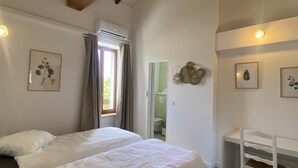 Un dormitorio con dos camas, un escritorio y una silla. Tiene un ventanal con cortinas, un aire acondicionado instalado en la pared e impresiones enmarcadas de plantas.