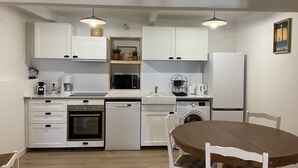 Una cocina compacta con gabinetes blancos, lavavajillas, horno, microondas, pileta y una mesa con sillas.
