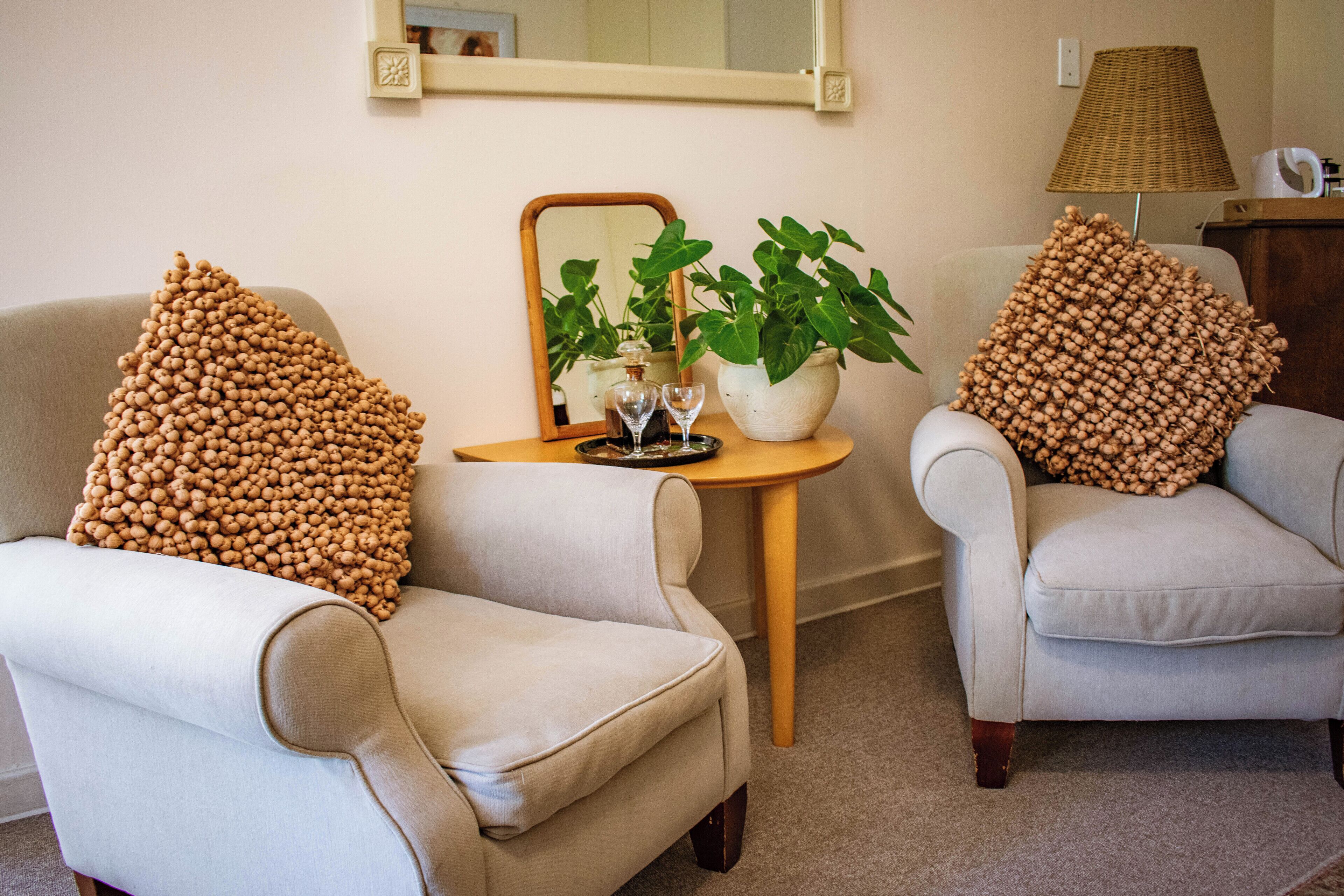Two armchairs with textured pillows, a small table with a plant and a wine glass, and a lamp on a wooden side table.