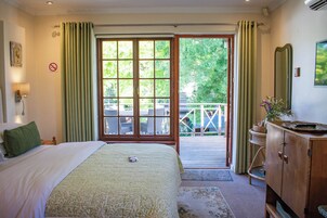 Un dormitorio con cama, cómoda de madera, espejo y vistas a un balcón con mobiliario exterior.