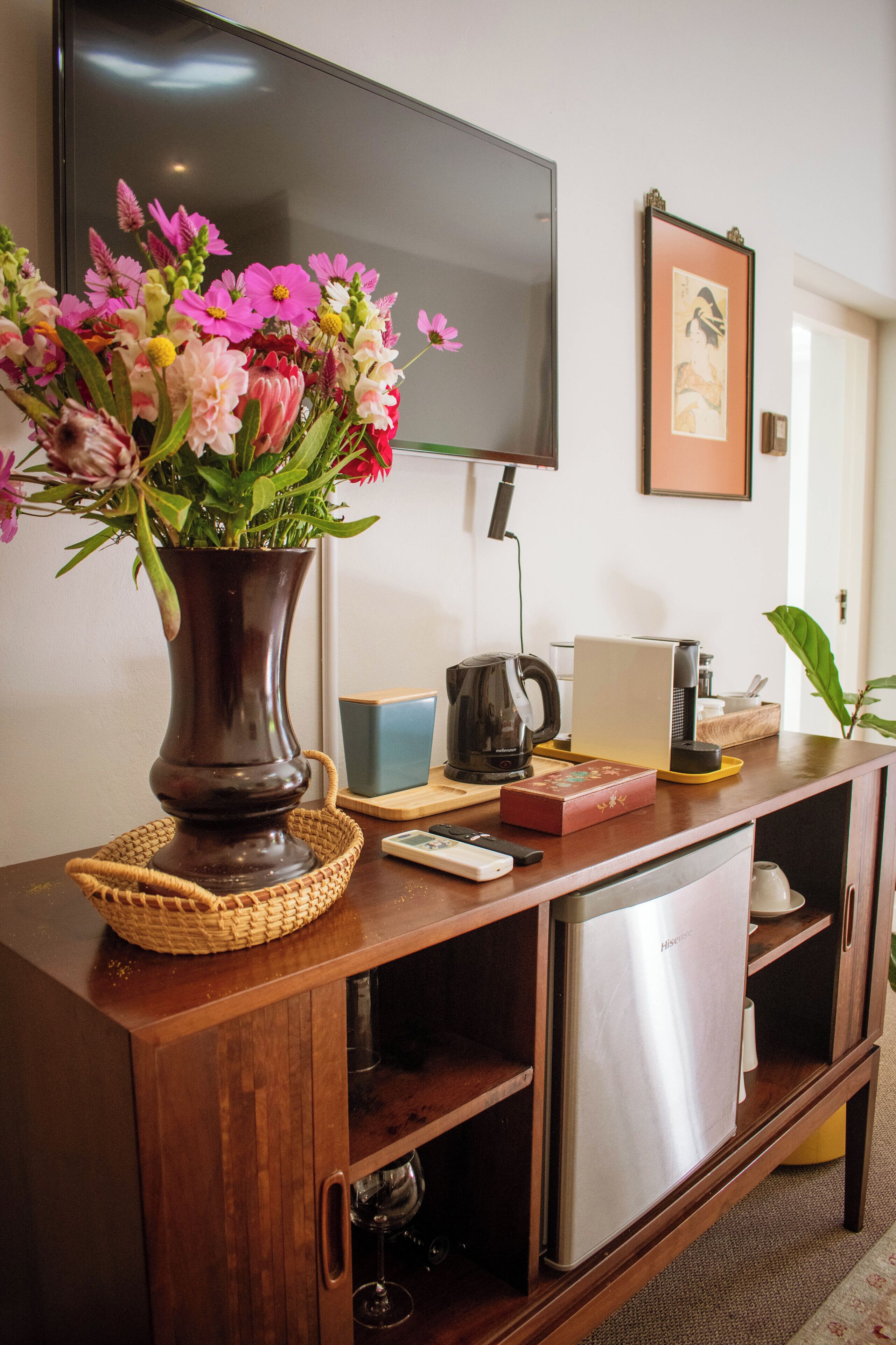 Una consola de madera con un florero, un televisor y varios objetos, incluyendo una cafetera y una caja.