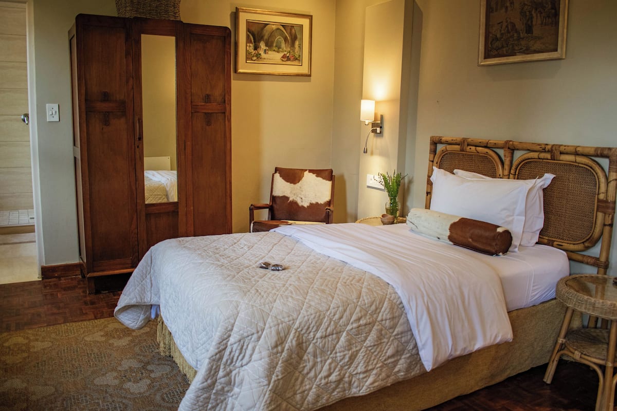 A neatly made bed with a quilt, a wooden wardrobe, a chair, and two wall-mounted lamps.