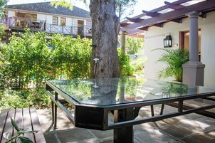 Una mesa con cubierta de vidrio en un patio, con un árbol y un edificio al fondo.