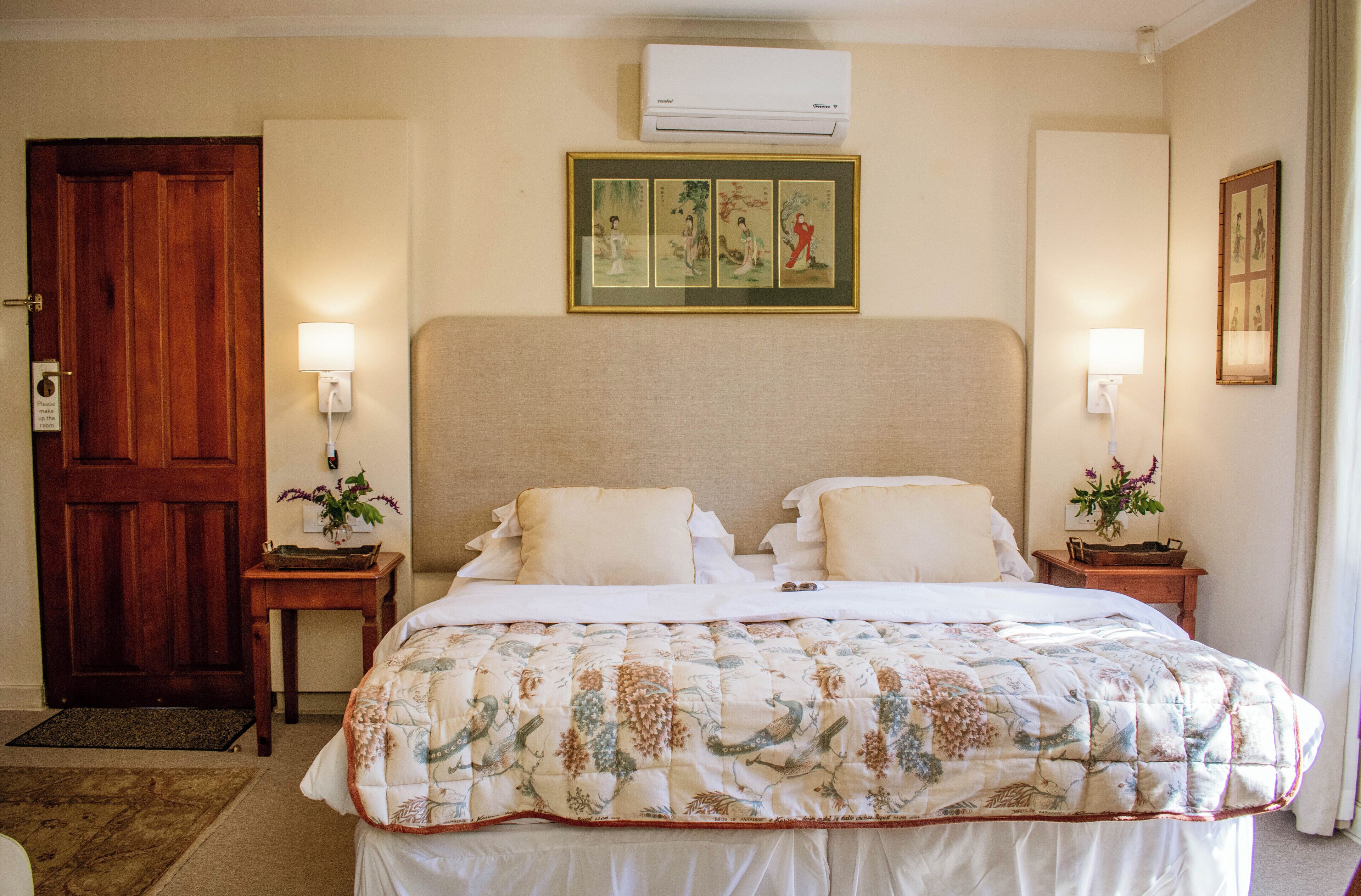A hotel room with a large bed, two bedside tables with lamps, a wooden door, and a wall-mounted air conditioner.