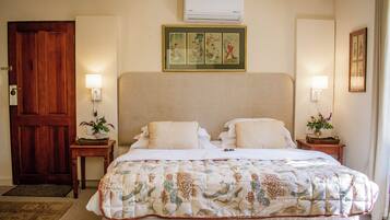 A hotel room with a large bed, two bedside tables with lamps, a wooden door, and a wall-mounted air conditioner.