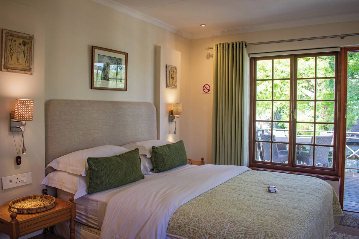 A hotel room with a large bed, two bedside tables, a window with a view of the outdoors, and wall-mounted artwork.