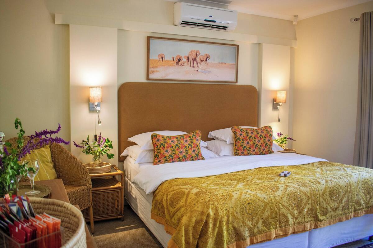 A hotel room with a large bed, a headboard, a wall-mounted air conditioner, and a painting of elephants.