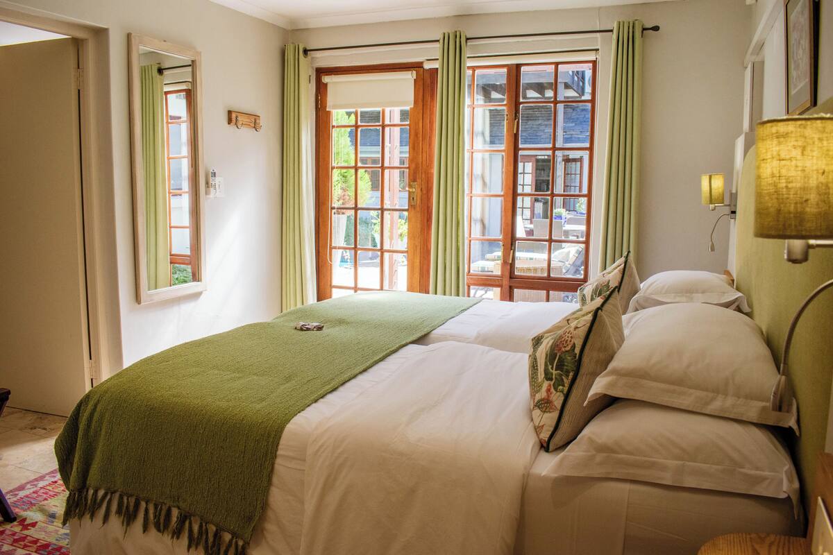 A neatly made bed with a green blanket, a bedside lamp, and a window with curtains.