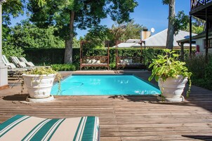 Una terraza de madera con piscina, sillas de descanso y plantas en macetas.