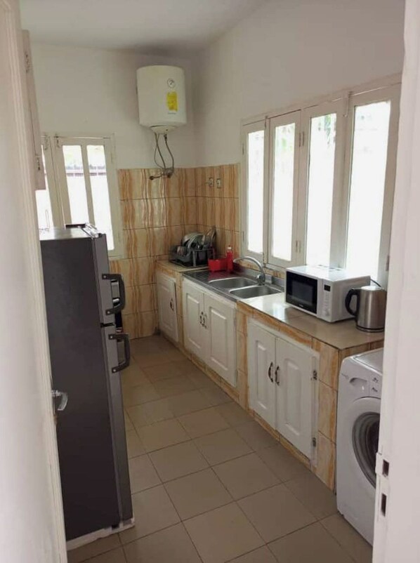 Una cocina con armarios blancos, microondas, lavadora y escurreplatos.