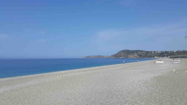 A beach with a clear sky and calm sea. There are boats on the water and a hill with buildings in the background. - Beachfront apartment on the western riviera (Milazzo)