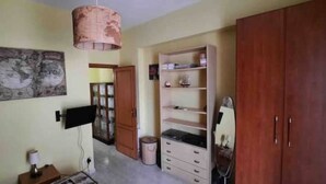 A room with a wooden wardrobe, a shelf unit, a hanging lamp, and a framed picture on the wall. - Beachfront apartment on the western riviera (Milazzo)