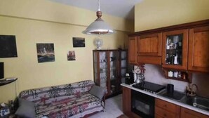 A compact living space with a sofa, a television, wooden cabinets, and a kitchen area. - Beachfront apartment on the western riviera (Milazzo)