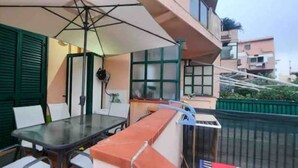 A balcony with a table and chairs, a fan, and a railing. - Beachfront apartment on the western riviera (Milazzo)