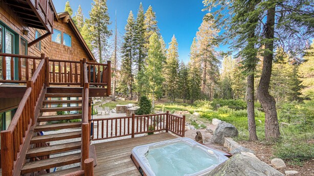 A wooden deck with a hot tub and a staircase leading to a cabin in a forest. - Silverado Lodge at Palisades - 4BR w/ Private Hot Tub, Ski Shuttle & Pet-Friendly! (Olympic Valley)