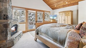 A bedroom with a stone fireplace, a bed with patterned pillows, a wooden wardrobe, and a television. - Silverado Lodge at Palisades - 4BR w/ Private Hot Tub, Ski Shuttle & Pet-Friendly! (Olympic Valley)