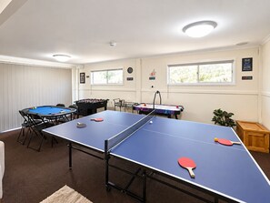 A room with a ping pong table, a foosball table, and a pool table.