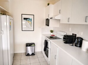 Une cuisine compacte avec des meubles blancs, un four à micro-ondes, une cuisinière, une poubelle et une machine à café.