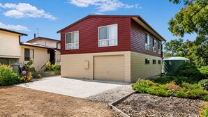 A two-story house with a garage, a driveway, and a garden with various plants. - Carlenes Getaway | Lake Views, Beach & Games Hub (Loch Sport)